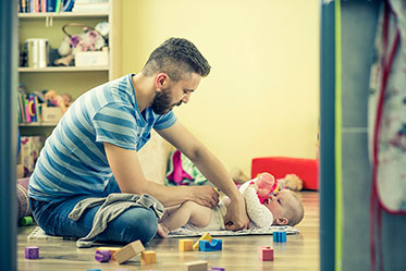 Vergrößerungsansichten für Bild: Nahaufnahme: Ein Vater wickelt auf dem Boden das Baby
