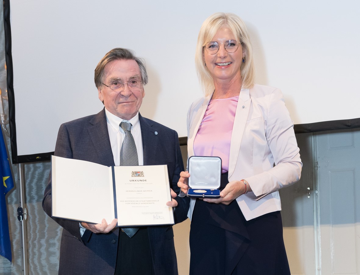 Das Foto zeigt: Elmar Wepper mit Bayerns Sozialministerin Ulrike Scharf bei der Verleihung der Staatsmedaille für soziale Verdienste am 25. April 2023.